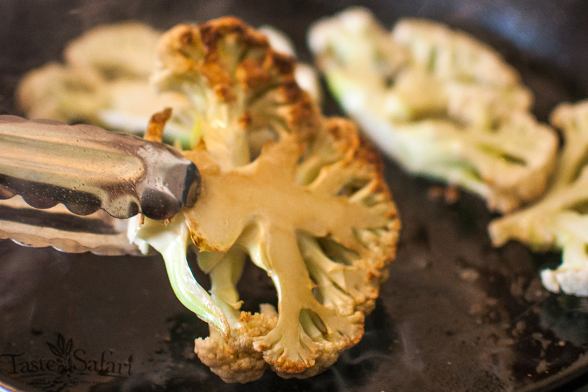 Searing a cauliflower steak in a pan held with tongs