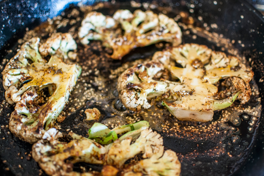 Golden seared cauliflower steaks with sesame seeds frying in a pan